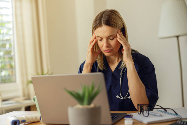 Tired female healthcare worker using laptop while working at doctors office - Foto, Imagen