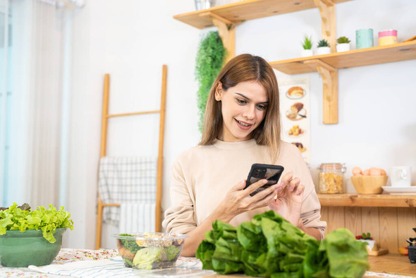 Young woman preparing healthy food with salad vegetables. woman sitting at pantry in a beautiful interior kitchen. The clean diet food from local products and ingredients Market fresh. - Photo, Image