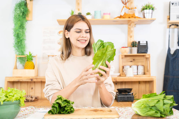 Mujer joven preparando alimentos saludables con verduras de ensalada. mujer sentada en la despensa en una hermosa cocina interior. La dieta limpia alimentos de productos e ingredientes locales. - Foto, Imagen