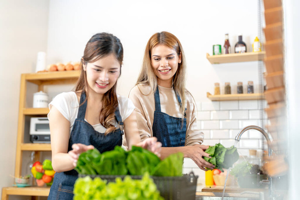 Χαμογελαστές γυναίκες που ετοιμάζουν φρέσκα υγιεινά λαχανικά σαλάτας. γυναίκα στέκεται στο ντουλάπι σε μια όμορφη εσωτερική κουζίνα. Η καθαρή διατροφή των τροφίμων από τοπικά προϊόντα και συστατικά. - Φωτογραφία, εικόνα