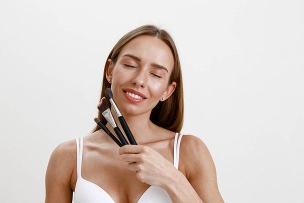 Young woman with healthy skin making makeup using cosmetic brush on studio background - Photo, Image