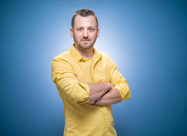 Bearded man posing while looking to camera over blue background, dresses in yellow shirt. Bearded guy. Studio shot - Фото, изображение