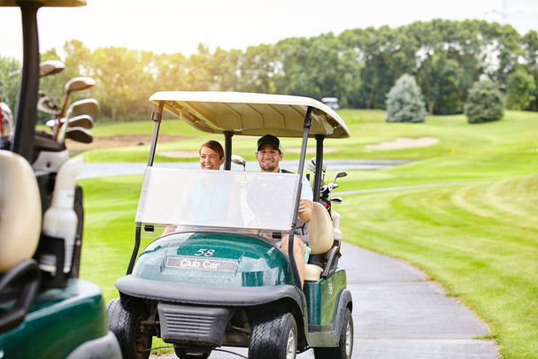 Were ready to step onto the green. a couple riding in a golf cart on a golf course - Фото, зображення