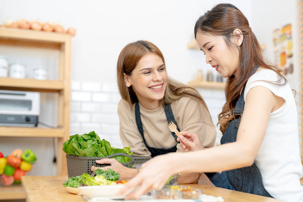 Lächelnde Frauen bereiten frisches, gesundes Salatgemüse zu. Frau sitzt an Speisekammer in einer schönen Innenküche. Die saubere Ernährung Lebensmittel aus lokalen Produkten und Zutaten Markt frisch. - Foto, Bild