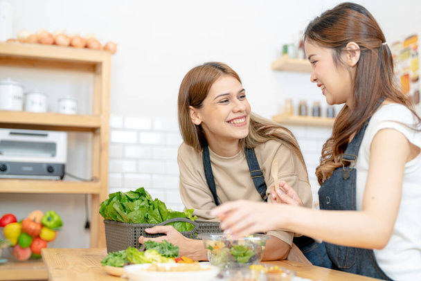 Χαμογελαστές γυναίκες που ετοιμάζουν φρέσκα υγιεινά λαχανικά σαλάτας. γυναίκα κάθεται στο ντουλάπι σε μια όμορφη εσωτερική κουζίνα. Η καθαρή διατροφή των τροφίμων από τοπικά προϊόντα και συστατικά. - Φωτογραφία, εικόνα