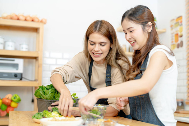 Χαμογελαστές γυναίκες που ετοιμάζουν φρέσκα υγιεινά λαχανικά σαλάτας. γυναίκα κάθεται στο ντουλάπι σε μια όμορφη εσωτερική κουζίνα. Η καθαρή διατροφή των τροφίμων από τοπικά προϊόντα και συστατικά. - Φωτογραφία, εικόνα