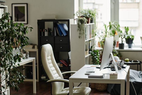 Рабочее место современного менеджера или креативного веб-дизайнера с компьютерным монитором, стоящим на столе с канцелярскими принадлежностями и креслом рядом - Фото, изображение