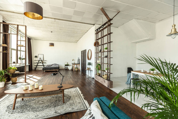 ευρύχωρο στούντιο διαμέρισμα διακοσμημένο με ξύλο και λευκό. Μινιμαλιστικός σχεδιασμός με τεράστια παράθυρα στο φως του ήλιου. κουζίνα και καθιστικό - Φωτογραφία, εικόνα