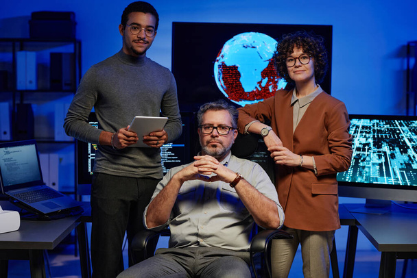 Gruppe dreier erfolgreicher interkultureller Programmierer blickt in die Kamera, während zwei junge Kollegen einen reifen IT-Ingenieur umgeben - Foto, Bild
