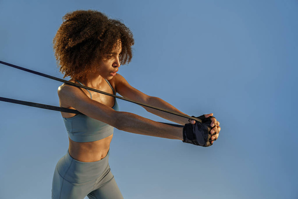 Сильна жінка в спортивному одязі виконує фізичні вправи з групою опору на студійному фоні
 - Фото, зображення