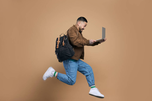 Профиль фото спортивного активного азиатского парня, прыгающего с ноутбука, наслаждаясь онлайн образование изолированный коричневый цвет фона  - Фото, изображение