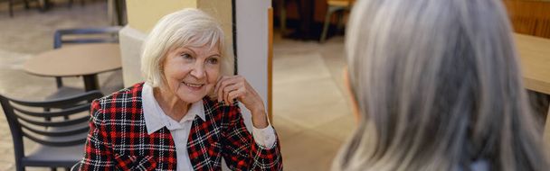 Ekose ceketli, güzel, yaşlı bir kadın kentteki kafe terasında uzun saçlı bir kadınla sohbet ediyor. - Fotoğraf, Görsel