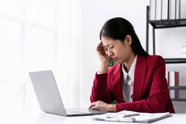 現代のワークスペースのテーブルで作業中にラップトップ上のキーボードで新しいビジネスと入力情報の会計について思慮深くしながら、ストレスや頭痛に合うビジネス女性. - 写真・画像