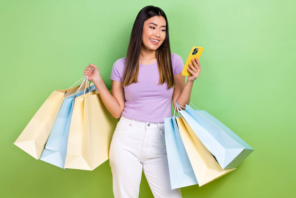 Photo of attractive japanese korean young woman hold device shopping bags wear trendy purple clothes isolated on green color background. - Fotografie, Obrázek