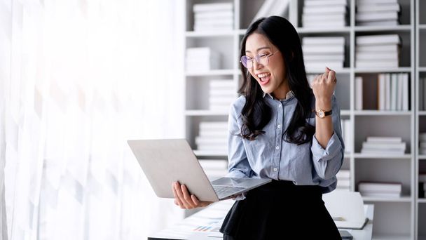 Accounting business concept, Accountant woman reads good news on laptop with excited and raising fist to celebrate achievement while working to typing about investment with business planning finance. - Photo, Image