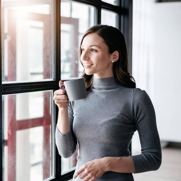 Conceito de estilo de vida acolhedor Empresária, Empresária bebendo chocolate quente e de pé perto da janela para olhar para fora para fazer uma pausa com desfrutar enquanto relaxa depois de trabalhar. - Foto, Imagem