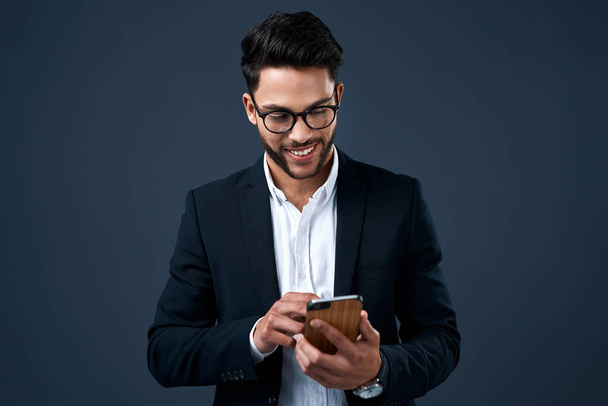 Bienvenidos a la era digital. un joven hombre de negocios guapo de pie solo contra un fondo gris estudio y mensajes de texto en su teléfono celular - Foto, Imagen
