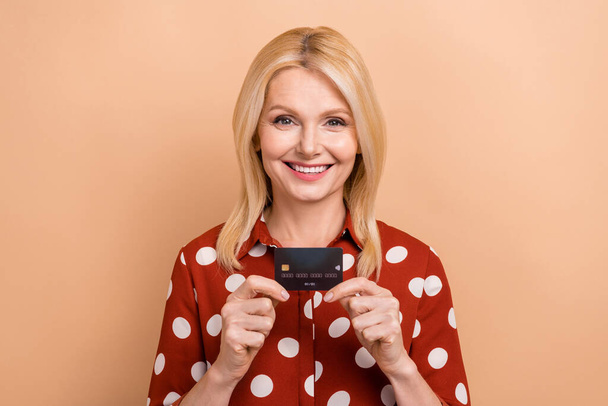 Photo of good mood senior woman with bob hairdo wear dotted shirt hold black plastic card isolated on pastel color background. - Fotoğraf, Görsel