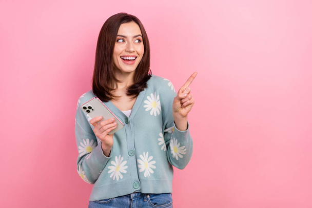 Photo of funny young girl direct finger empty space using apple smartphone wear cardigan app store isolated on pink color background. - Foto, immagini
