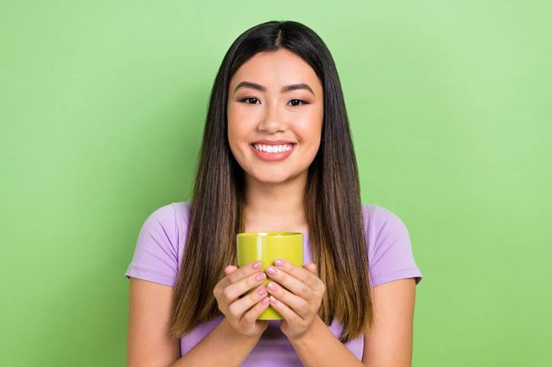 Photo portrait of pretty japanese korean young girl hold tea coffee mug smile wear trendy purple outfit isolated on green color background. - Foto, imagen