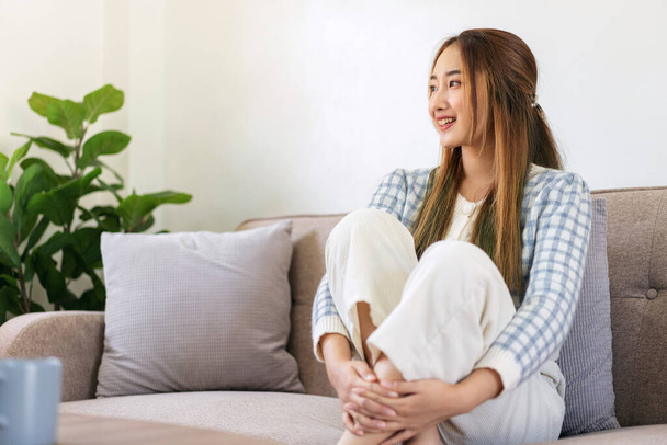 Woman enjoying dreamy and relaxing with looking outside while sitting on the comfortable sofa to leisure with cozy lifestyle in living room at home. - Photo, Image