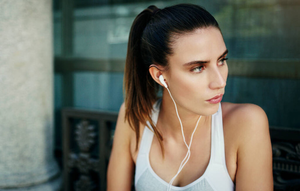 Ό, τι νομίζεις, γίνεσαι. μια νεαρή γυναίκα που ακούει μουσική κατά τη διάρκεια της προπόνησής της στην πόλη - Φωτογραφία, εικόνα
