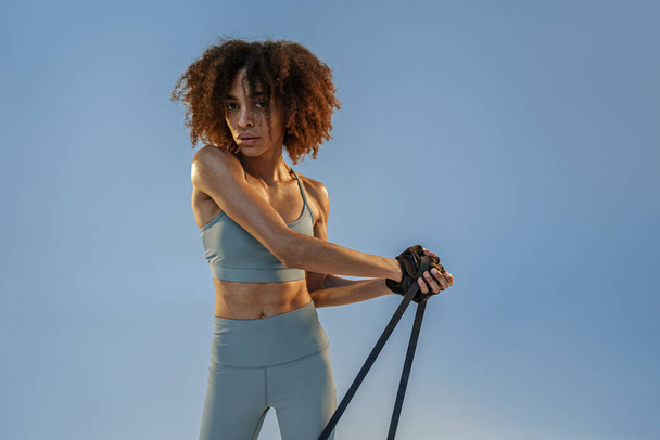 Woman performs exercises with expander on studio background. Strength and motivation - Fotó, kép
