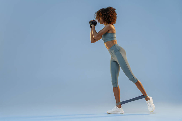 Athletic woman trains legs with fitness elastic band on studio background. High quality photo - Φωτογραφία, εικόνα