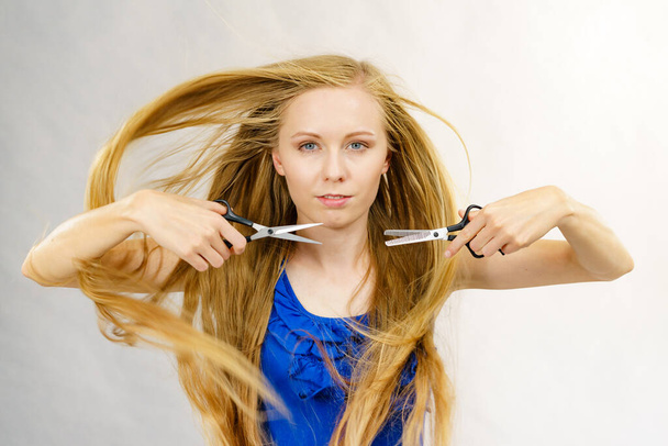 Haircut coiffure haircare concept. Girl with blowing long blond hair holding scissors, showing work tools, normal and thinning shears. - Zdjęcie, obraz