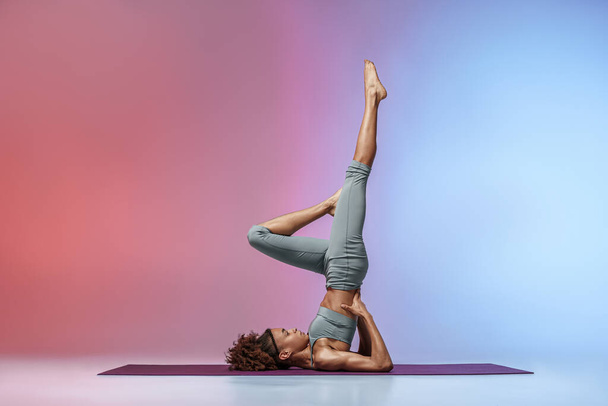 Fitness woman practicing yoga on mat on studio background with color filter. High quality photo - Φωτογραφία, εικόνα