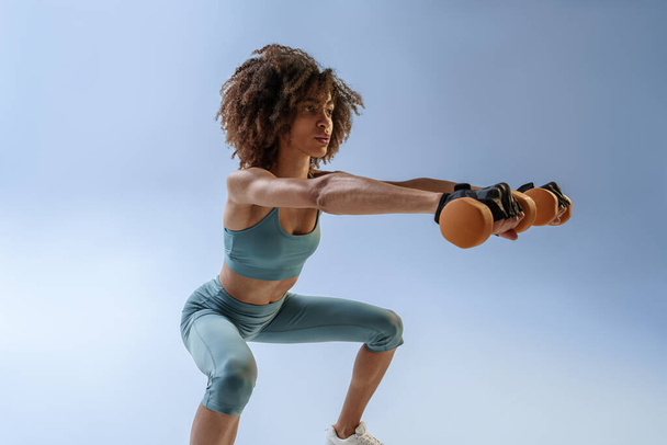 Egy nő, aki súlyzókkal gyakorol a stúdió hátterében. Sport és egészséges életmód - Fotó, kép