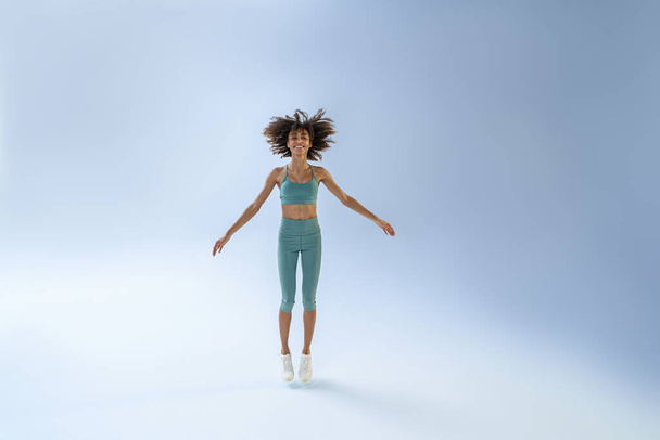 Athletic active woman jumping on studio background. Dynamic movement - Foto, afbeelding