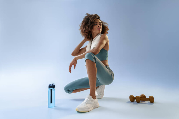Woman with bottle of water and dumbbells after gym, resting on studio background. High quality photo - Foto, Imagem
