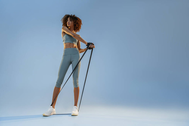 Woman performs exercises with expander on studio background. Strength and motivation - Foto, imagen