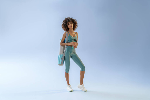Donna con borsa sportiva e bottiglia d'acqua dopo l'allenamento su sfondo studio. Foto di alta qualità - Foto, immagini
