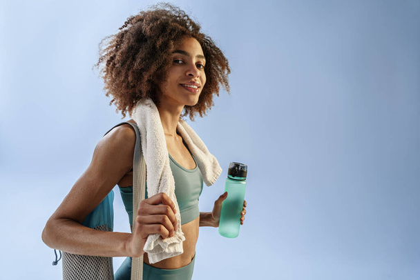 Woman with sports bag and bottle of water after training on studio background. High quality photo - Fotografie, Obrázek