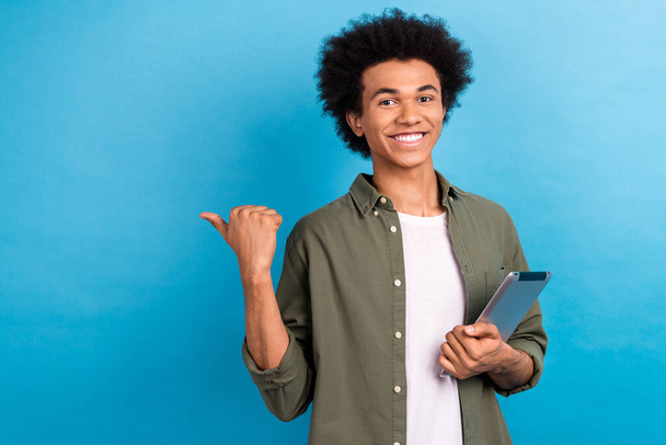 Fotografie mladého studenta chlap držet nové zařízení tablet ukazující prstem prázdný prostor promotér ekommerce produkt izolované na modrém pozadí. - Fotografie, Obrázek