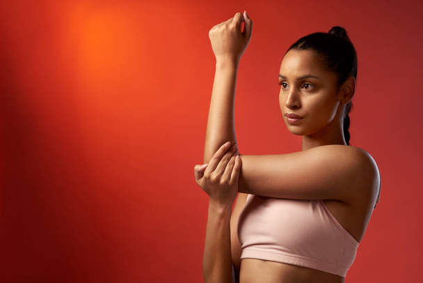 Push your mind so you can push your body too. Studio shot of a sporty young woman stretching her arms against a red background - Photo, Image