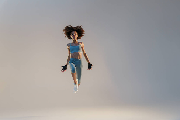 Athletic active woman jumping on studio background. Dynamic movement - Фото, изображение