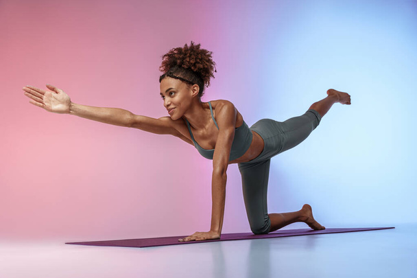 Fitness woman practicing yoga on mat on studio background with color filter. High quality photo - Foto, Imagem