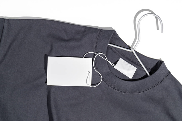 Graues T-Shirt mit Preisschild oder Etikettenattrappe auf einem Kleiderständer. Ökologiekonzept. Bekleidungsverkaufskonzept - Foto, Bild