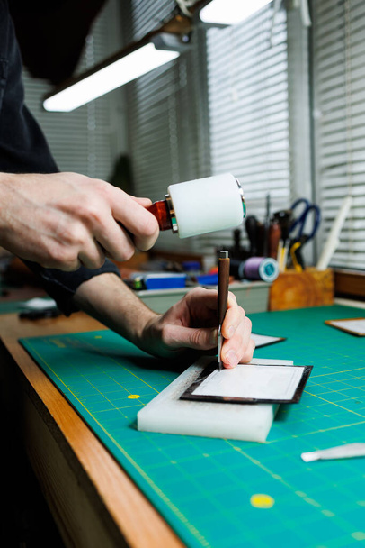Die Hände eines professionellen Handwerkers machen aus einer Ledertasche eine neue, saubere, echte Ledertasche, Nahaufnahme-Schnappschuss. - Foto, Bild