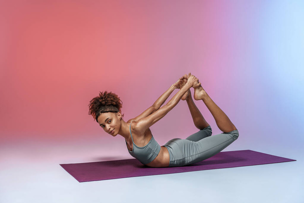 Athletic woman in sportswear doing stretching exercises on yoga mat on studio background  - Zdjęcie, obraz