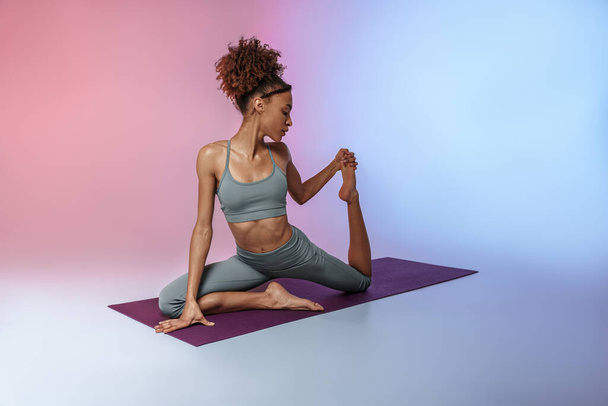 Fitness woman practicing yoga on mat on studio background with color filter. High quality photo - Foto, afbeelding