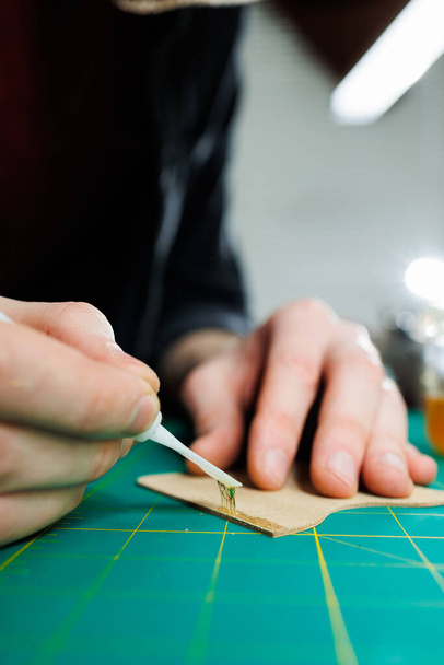 Ruce mistra šijeme ručně vyráběné kožené výrobky. Pánské ruce spojují díly a vytvářejí kvalitní kožené doplňky. Pracovní proces v kožené dílně - Fotografie, Obrázek