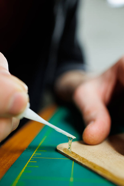 Las manos del maestro cosen productos de cuero hechos a mano. Las manos de los hombres conectan las piezas, creando accesorios de cuero de calidad. Proceso de trabajo en un taller de cuero - Foto, Imagen