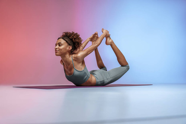 Athletic woman in sportswear doing stretching exercises on yoga mat on studio background  - Photo, Image
