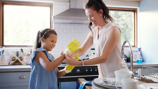 These gloves are a must honey. an affectionate young mother helping her daughter to put on rubber gloves while doing the dishes at home - 写真・画像