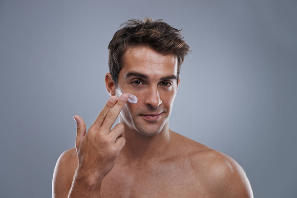 Even men like to be soft....Studio shot of a handsome young man applying cream to his face - Foto, afbeelding
