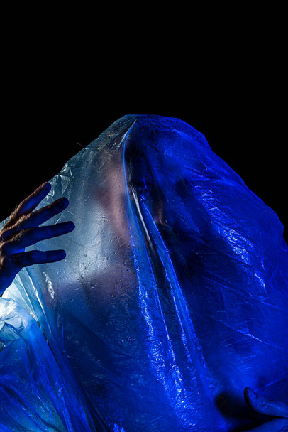 Man with plastic bag over his head, suffocated. Studio shot with blue filter. Isolated on black background. - Photo, Image